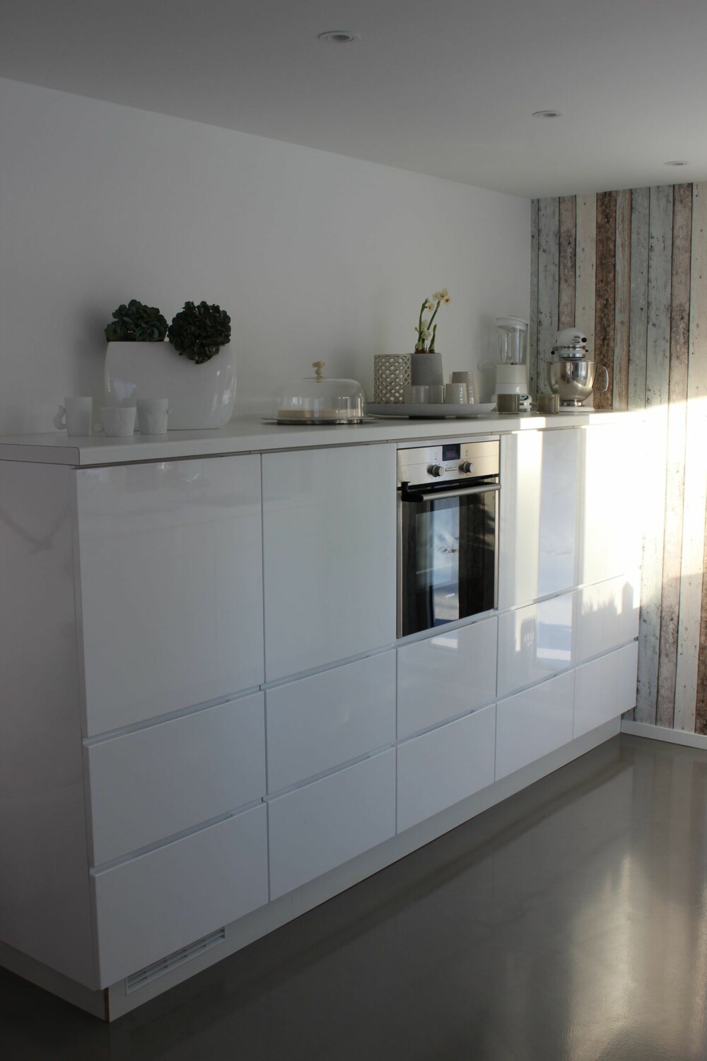 Kjøkken med moderne hvite fronter står i kontrast til den rustikke veggen med panellignende tapet.