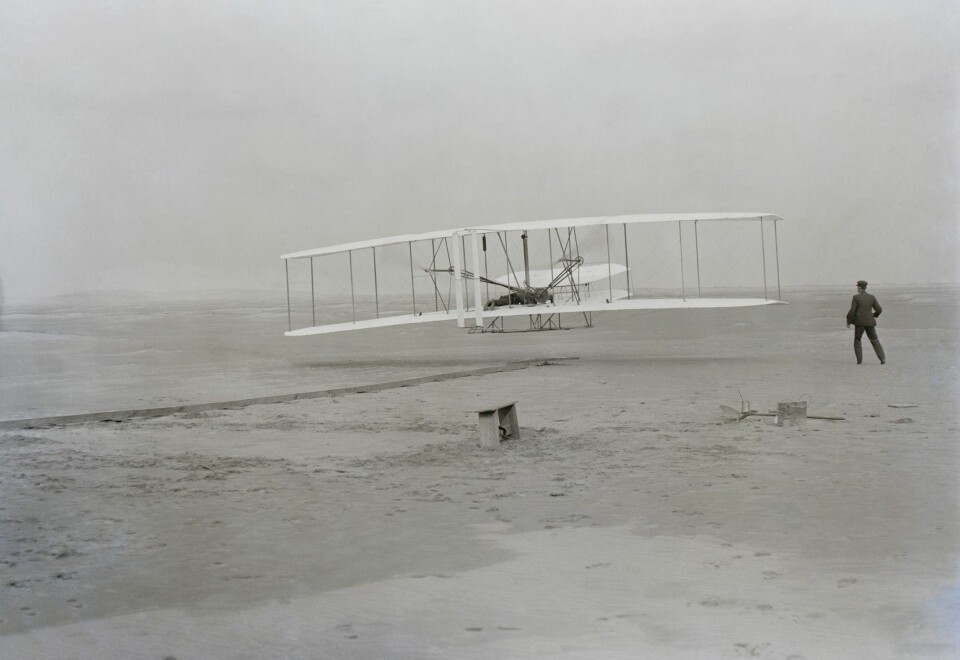 LUFTBÅRNE: Wilbur Wright løper ved siden av hans bror Orville som styrer flyet idet den letter på Wodden Track på Kitty Hawk. Dette var det første menneskestyrte flyet.
