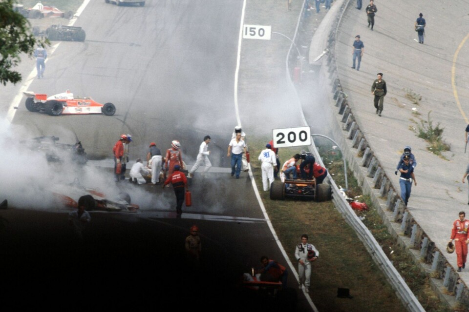 MASSEKRASJ: Den svenske Lotus-føreren Ronnie Peterson ligger på banen med knuste ben etter at han er blitt trukket ut av sin brennende Lotus 78 etter et massekrasj under Italia Grand Prix i 1978. Italieneren Vittorio Brambilla sitter fast i bilen til høyre (under 200-skiltet). Peterson dør senere av en blodpropp under en operasjon på sykehuset.