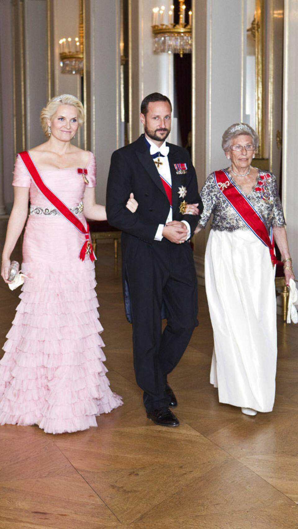 Kronprinsesse Mette-Marit, kronprins Haakon og prinsesse Astrid på vei inn til slottsmiddag for stortingsrepresentantene i oktober 2010. Her iført en rosa kjole fra Emilio Pucci.