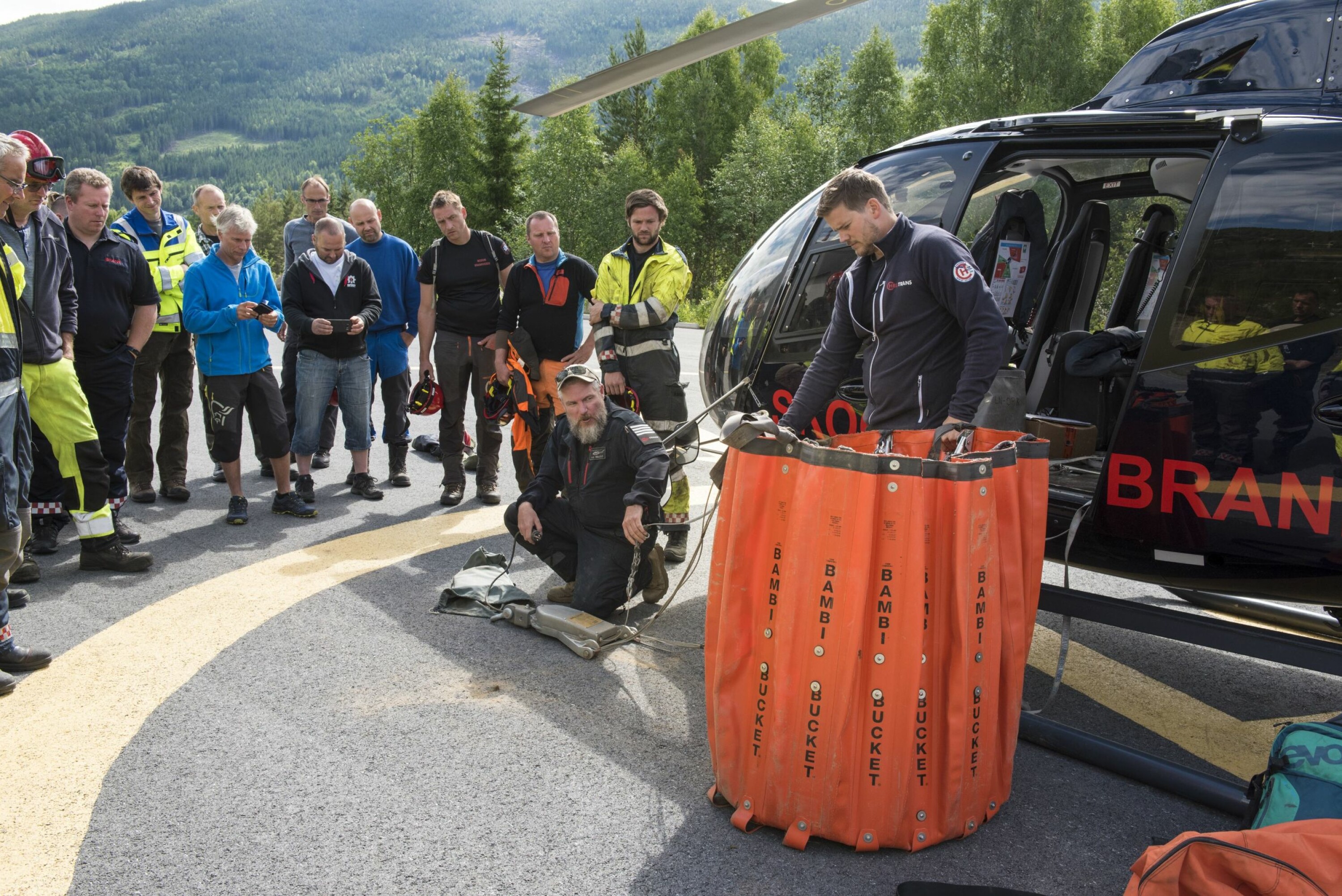 SAMARBEID: Pilot John-Arne Hellesø og lastemann Nils Martin Holden demonstrerer vannbøtta for brannfolk i Hallingdal.