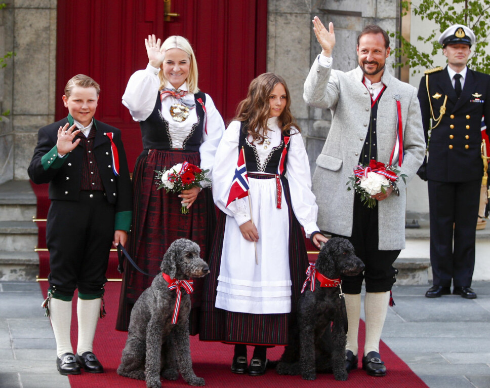 BUNADSKLEDDE: Kronprinsfamilien hilser barnetoget på Skaugum 17. mai 2018. Fra venstre prins Sverre Magnus (med hunden Muffins Kråkebolle), kronprinsesse Mette-Marit, prinsesse Ingrid Alexandra (med hunden Milly Kakao) og kronprins Haakon. Sverre Magnus, Mette-Marit og Ingrid Alexandra er alle ikledd Vest-Agderbunad, mens kronprins Haakon går i Askerbunad.