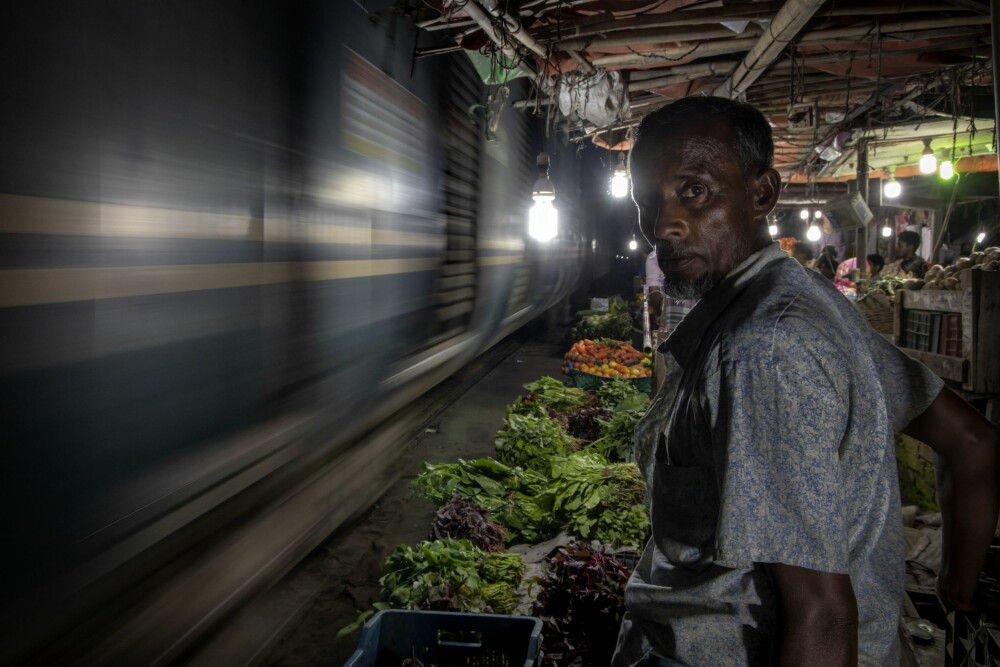 <b>DUNDRER FORBI:</b> Grønnsaksselger Mohidul venter tålmodig mens et tog passerer i høy fart. Han rakk akkurat å flytte boden sin før toget kom.