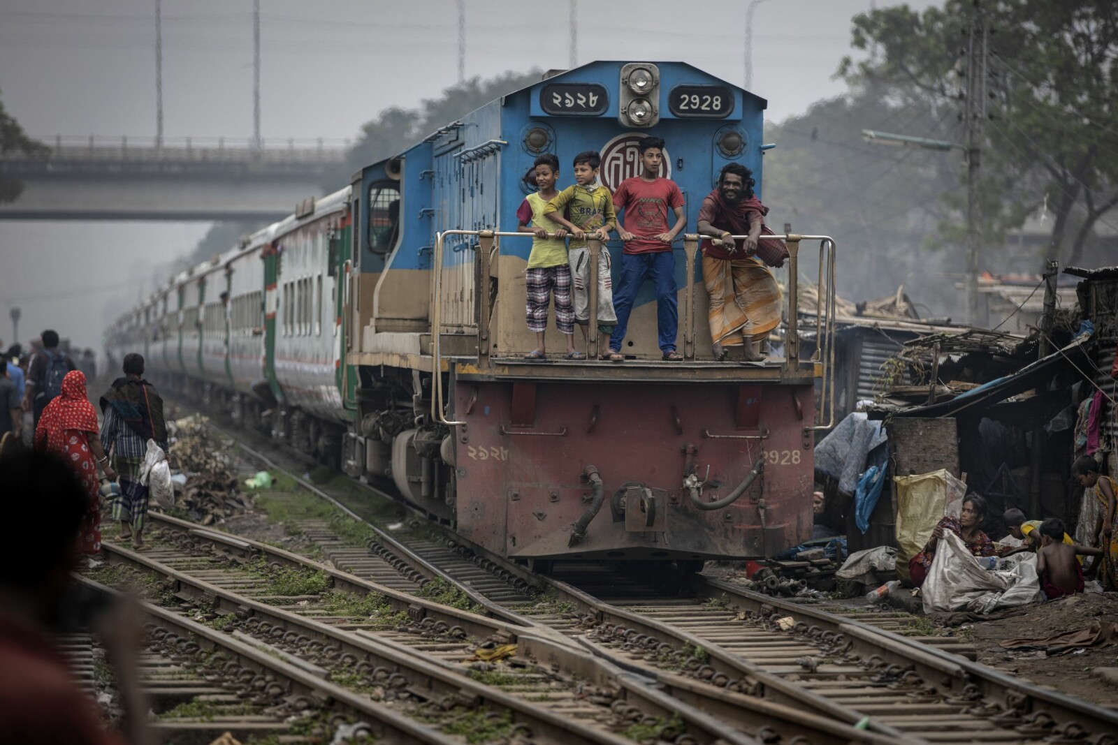 <b>UNNGÅR Å BETALE:</b> Tog er for mange det eneste transportalternativet når de skal til og fra jobb. Men noen ganger er det fullt og da benytter mange taket og andre plasser på toget. Men jeg ble fortalt at også mange fattige, som ikke har råd til billett, sniker ved å stå på taket eller som her; stå helt foran på loket. Noe de for øvrig så ut til å nyte, der toger farer gjennom slummen i Dhaka.