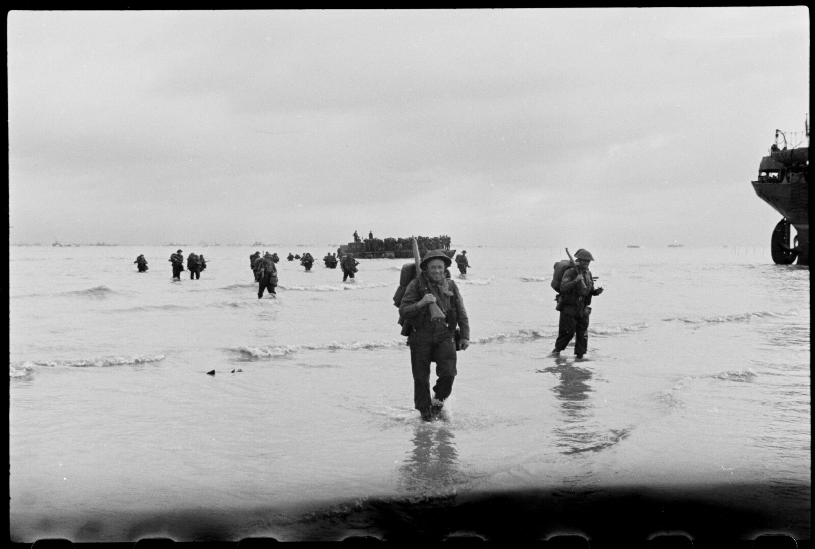 <b>LANDGANG:</b> Britiske soldater vasser i land på Juno Beach ved Berniéres-sur-Mer 7. juni 1944. «Vestmandrød», båten Ole Friele Backer kom med, skimtes til høyre.