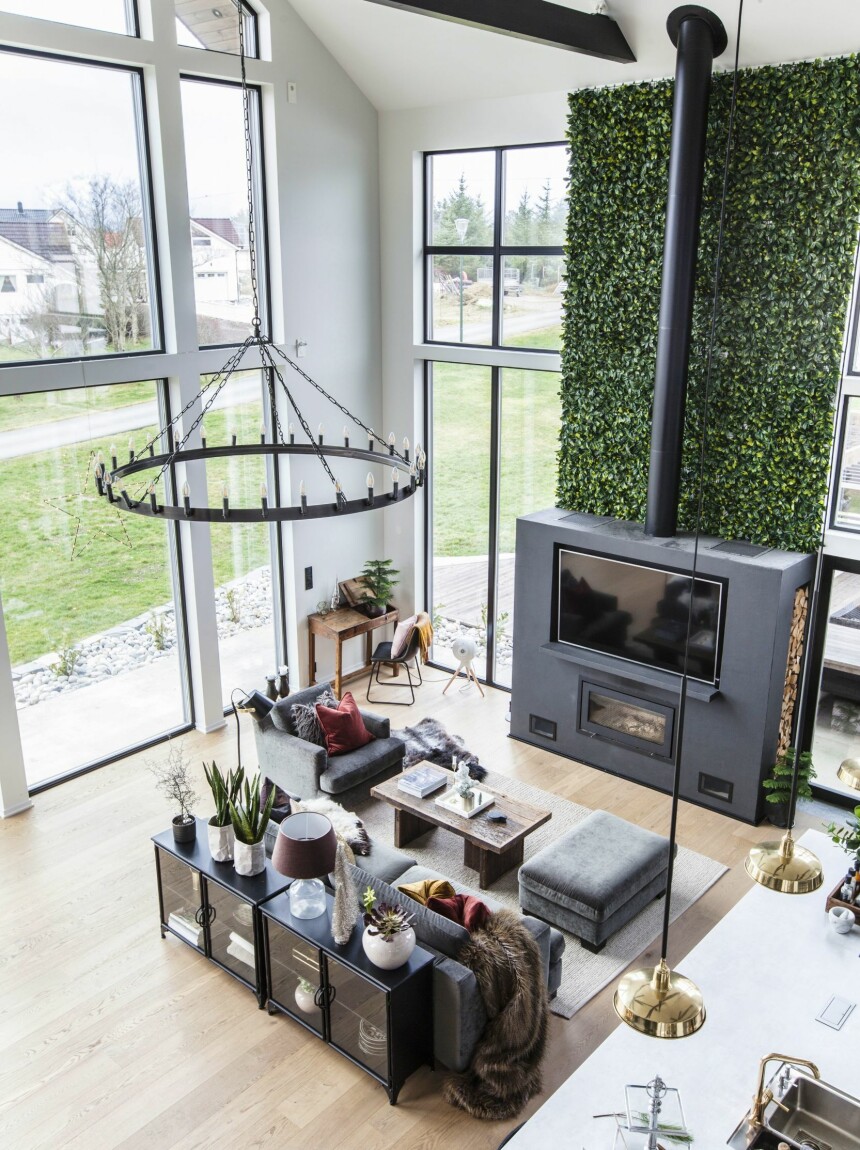 KOSELIG MED PEIS ... OG TV: Den vanvittige takhøyden på ni meter gir en luftig følelse i det store allrommet. De store vindusflatene tar inn mye lys og gir god utsikt mot havet. Peisen er bygget på stedet av Smartvarme Bergen, og familien måtte ha elektrikerhjelp for å få koblet til tv-en. Den grønne planteveggen over peisen er fra Ambiplants og er bygget opp av kunstige blader på 50 x 50-plater. Jernskapet foran sofaen og skrivebordet er fra Trademark. Teppet er fra Home & Cottage.