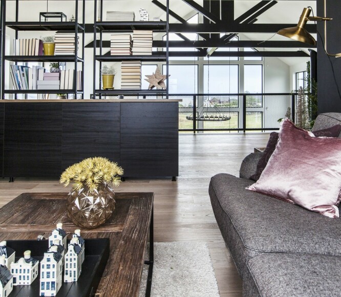 TILBAKETRUKKET MED UTSIKT: Fra mesaninen har man god utsikt ut mot fjorden. Rekkverket og mesaninen er laget i Polen, fraktet i deler og skrudd sammen på stedet. Hylleløsningen mellom sofaen og kontoret er en kombinasjon av Ikea-skap og hyller fra Skeidar, og fungerer som romdeler. De sorte bjelkene i taket endret de farge på etter at eieren av Hellvik Hus Sotra var på søndagstur. Han så dem og sa ganske bestemt at de må være svarte.