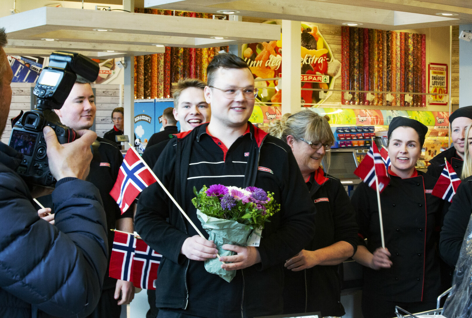 bilde av Sondre Guttormsensom akkurat har fått prisen som Landets hyggeligste kassamann. Her på Eurospar i Tromsø hvor han er omringet av kollegaer og fotografer