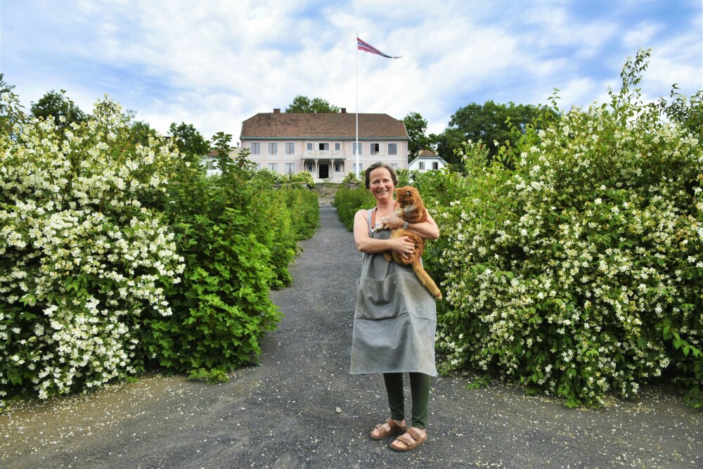 <b>VELKOMMEN:</b> Ma­ri­an­ne og gårdspusen, her inn­hyl­let i den dei­li­ge duf­ten av sjas­min, ønsker deg velkommen på omvisning i den historiske hagen deres.