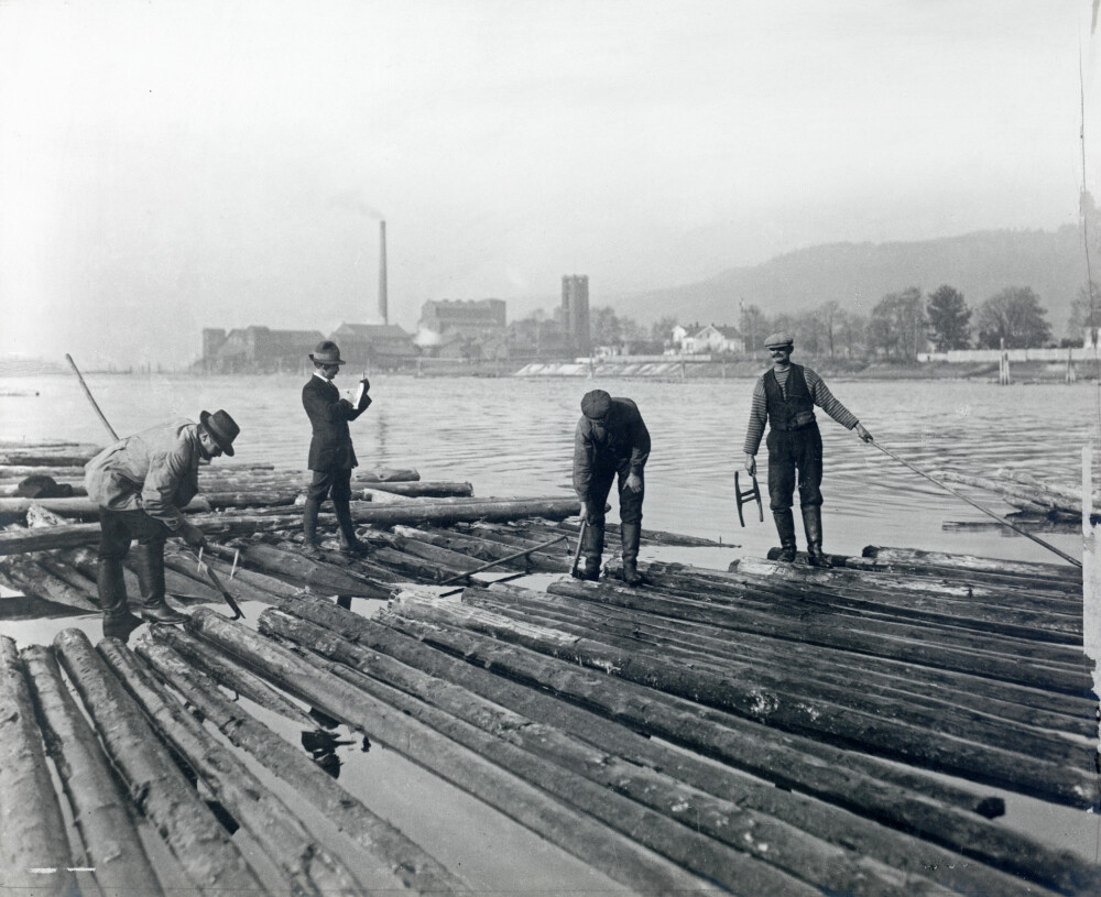 <b>OVERKLASSEN:</b> Tømmermåleren (nr. to fra høyre) utgjorde tømmerfløtingens overklasse. De tjente mange ganger mer enn fløterne ute i elven, her i Drammenselva i 1914.