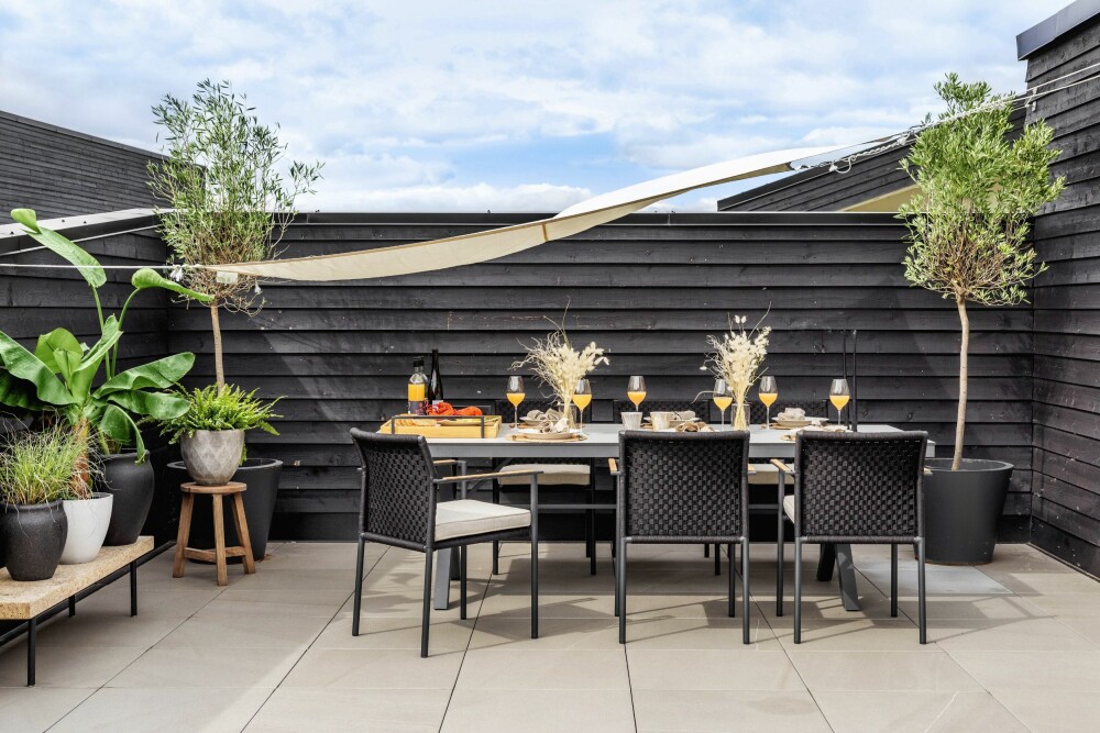 Den store terrassen utenfor kjøkkenet er et perfekt sted for gode måltider, og da særlig under det praktiske solseilet fra Rustibust. Bordet er fra Fresh Living, stolene fra Slettvoll og den lave benken fra Ikea.