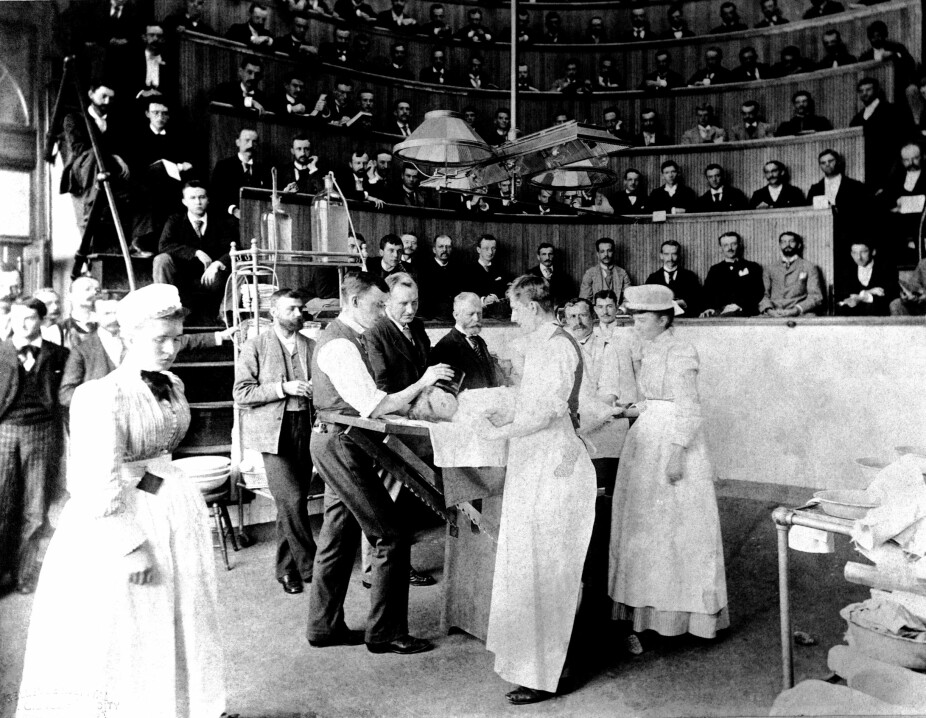 PÅ OPERASJONSBORDET: Dette bildet fra Bellevue Hospital and Anatomical Theater i New York, 1899, viser et lite menneske på operasjonsbenken og medisinsk personell foran en stor forsamling i anatomisalen.