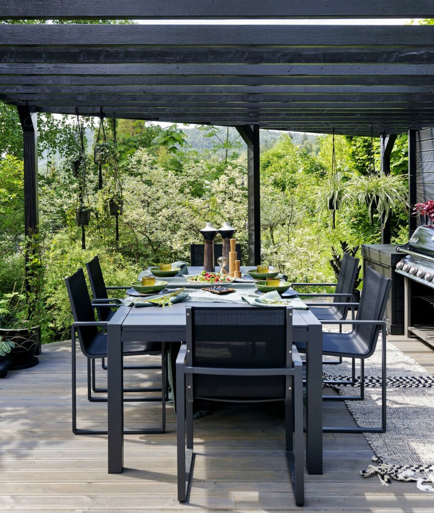 MIDDAG I DET FRI: Pergolaen forlenger sommersesongen i begge ender. Til høyre utekjøkkenet, som Kristian og Siri har laget selv. Spisebordet og stolene er fra Fine Design. Plantene som gir den deilige eksotiske stemningen er fra Kirsten Westergaard. Det vakre terrassegulvet heter Duo Alvdal Royal Fjellgrå og er kjøpt hos Alvdal Skurlag. Det er behagelig å gå på, noe som var et kriterium for Siri og Kristian – de vil kunne gå barbent ute.
