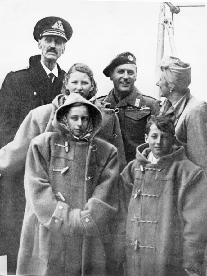 <b>GJENFORENT:</b> Smilende kronprins Olav og kronprinsesse Märtha sammen med kong Haakon. Dessuten prinsessene Ragnhild og Astrid og prins Harald, alle iført duffelcoat. De er om bord på krigsskipet «Norfolk» før ankomst til honnørbrygga i Oslo 7. juni 1945. 