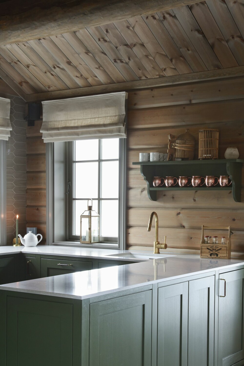 Over den praktiske kjøkkenøya henger en nostalgisk og klassisk vegghylle mot tømmerveggen. Dette skaper et klassisk og vakkert uttrykk i kombinasjon med den friske grønnfargen og kobbermuggene. 