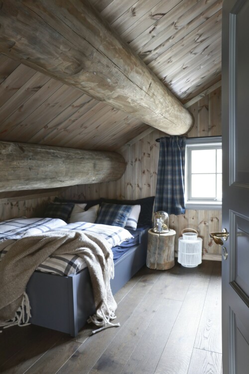 Soverommene oppe fungerer som gjesterom. Her er det innredet i blå valører med tekstiler fra Home &amp; Cottage. Nattbordet er laget med rester fra bjelkene i taket. 