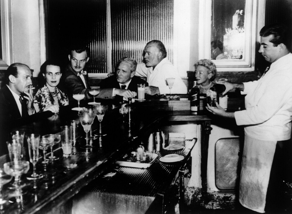 <b>CAFé FLORIDITA:</b> Legendariske Floridita i Havana, daiquiriens vugge og Hemingways absolutte favorittbar. Her sitter han (i hvitt) på sin faste plass sammen med bl.a. Spencer Tracy (rett foran ham) under filmati­seringen av «Den gamle mannen og havet» i 1958.