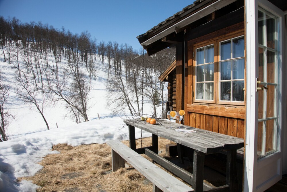 Etter en skitur kan påskesola nytes på uteplassen utenfor hovedhyttas tilbygg. Både kledning, vinduer <br/>og vindusomrammingen er behandlet med tjære. 