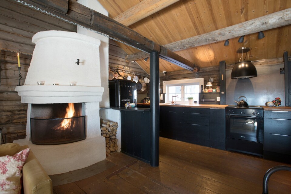 Kjøkkenet har en langsgående innredningsløsning uten bruk av overskap. Dette ble utført av forrige eier. Vennefamiliene har supplert med et lite, parallellgående parti mot peisen. De moderne frontene gir tøff kontrast til de gamle tømmerveggene. Bak kokesone er veggen kledd med en røff stålplate. Dette er gjort for å lette renholdet i sprutsonen. Ventilatoren og kjøleskapet understreker det bevisste spillet med moderne design og nostalgi. Innredningen er fra Ikea, ventilatoren fra Eico, kjøleskapet fra Smeg.