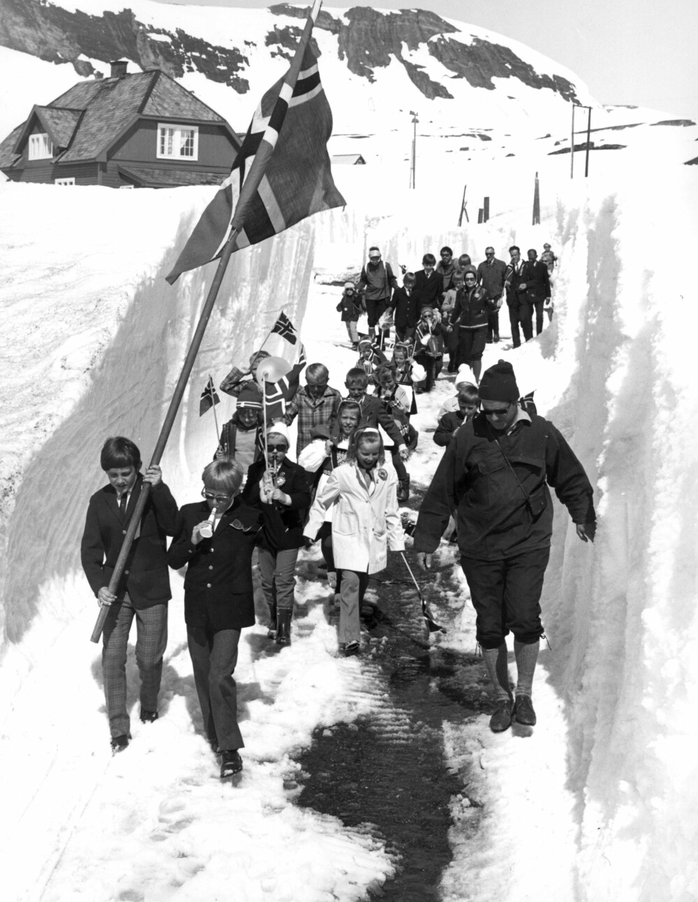 <b>LIKE BLIDE:</b> Norge har mye vær og klima. Her 17. mai på Finse i 1972. Høye brøyte­kanter og smal vei, men i barne­toget er alle like blide.