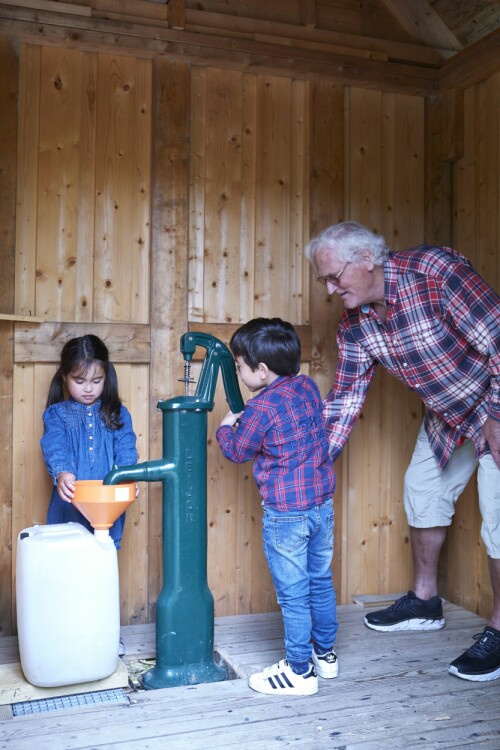 Vannhenting i pumpehuset med bestefar. Det er gøy å være med og hente vann synes Tim og Tia. Pumpehuset deler familien med flere hyttenaboer.