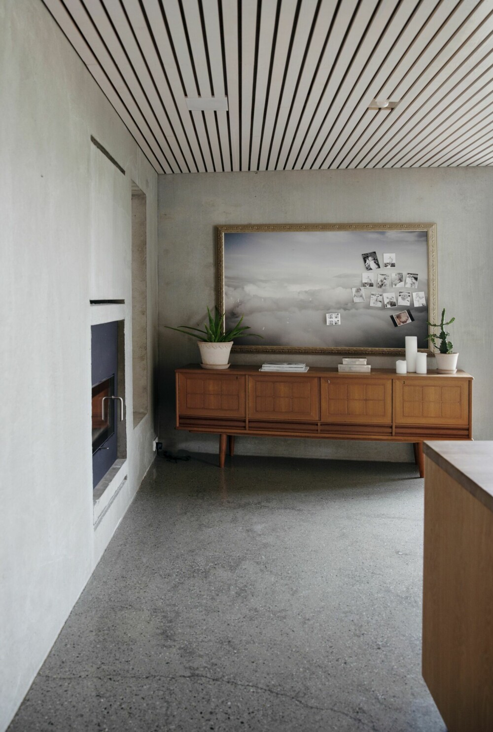 Ved den gjennomgående peisen, på kjøkkensiden, står en vakker skjenk med en del tiår bak seg. Den varme trefargen på møbelet blir understreket av de grå tonene på vegger og gulv.