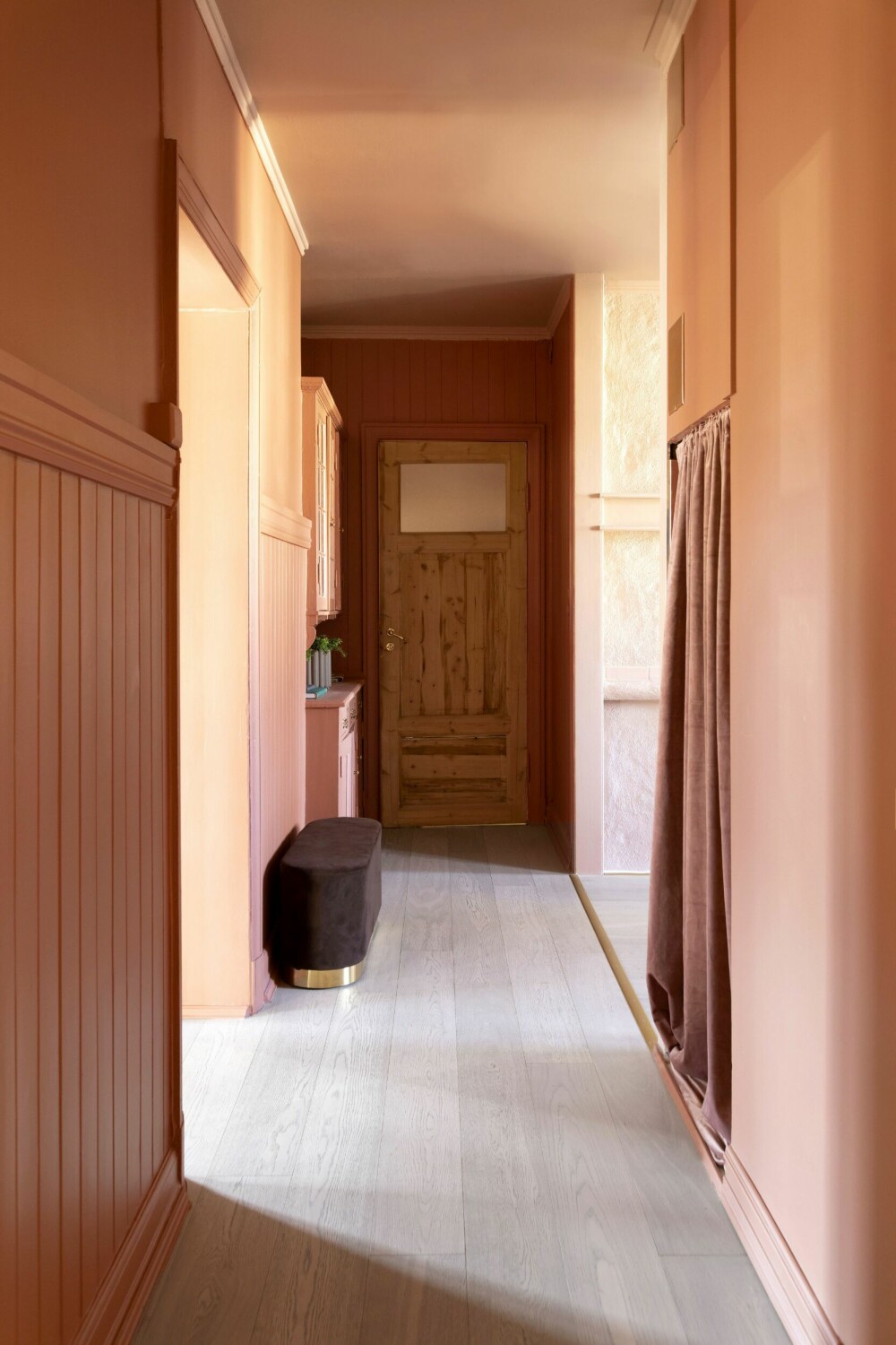 Den brunrøde gangen, malt i Lively Red fra Jotun, setter tonen i det man kommer inn i leiligheten, og den binder sammen palettens mange farger. Til høyre er åpningen inn mot kjøkkenet, mens stue og spisestue ligger til venstre. 