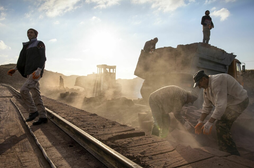 SOL ER UVÆR: Arbeiderne foretrekker faktisk dager med regn og sludd, fremfor sol og tørt. − Straks det er litt sol, tørker bakken opp umiddelbart og støv fyller lufta, forteller Solli, en av de eldre arbeiderne. Her lesser mennene steiner på en lastebil.