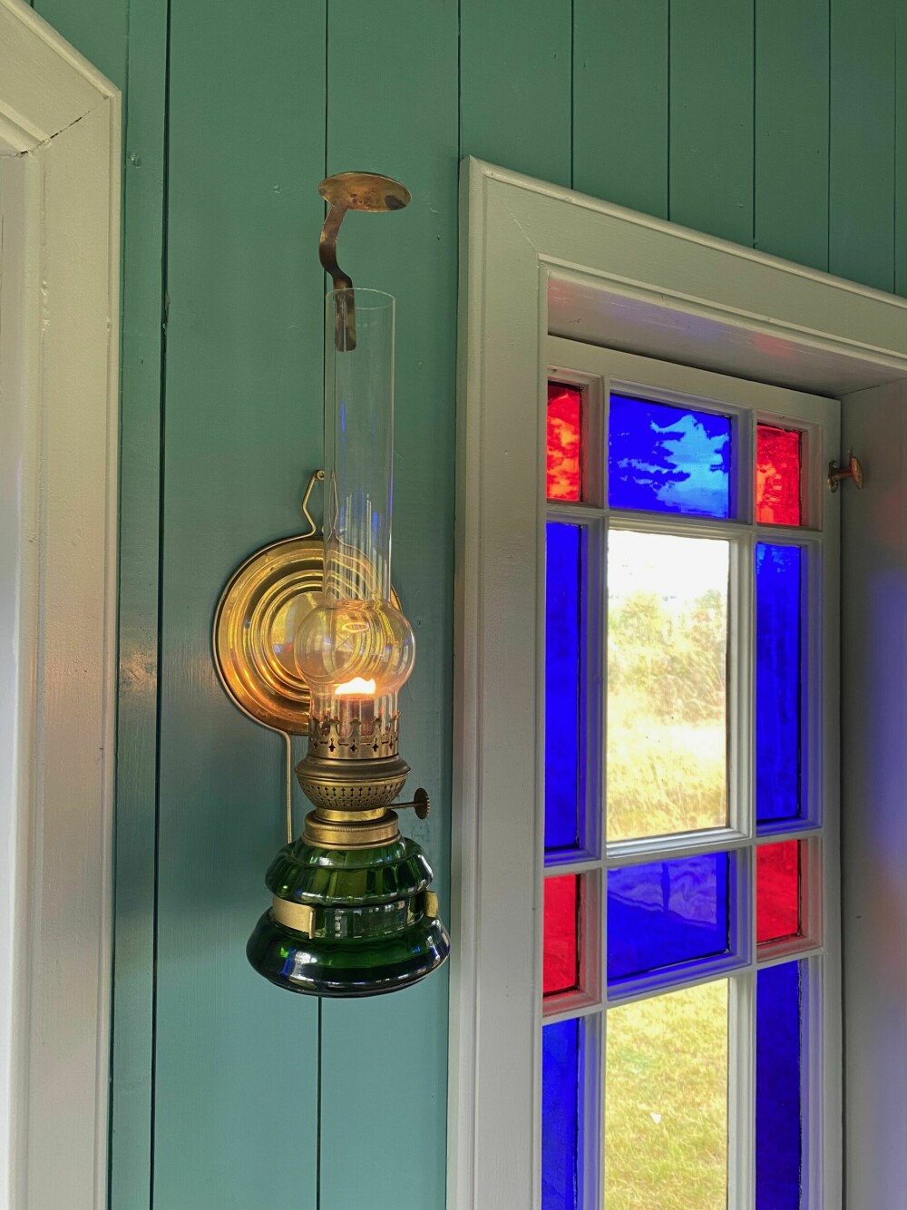 PARAFINLAMPE: En vakker og enkel vegghengt parafinlampe. Disse fantes det mange av rundt om i norske hjem. De ble stort sett produsert i gjennomsiktig glass, eller i grønt som her. De fantes også i porselen. Denne er helt komplett med den lille sotfangeren i toppen av glasset.