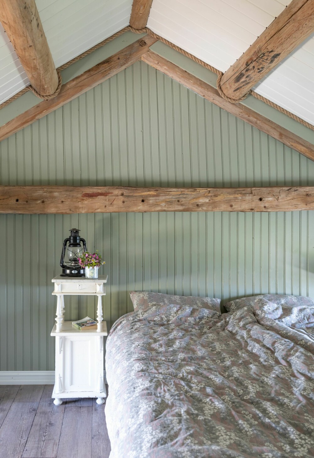 Tømmerfargen på de gamle, originale stokkene er naturelle. De er beholdt som en røff kontrast til de mer duse fargene. Det hvite taket og kommoden er en frisk kontrast til den grønne veggen.
