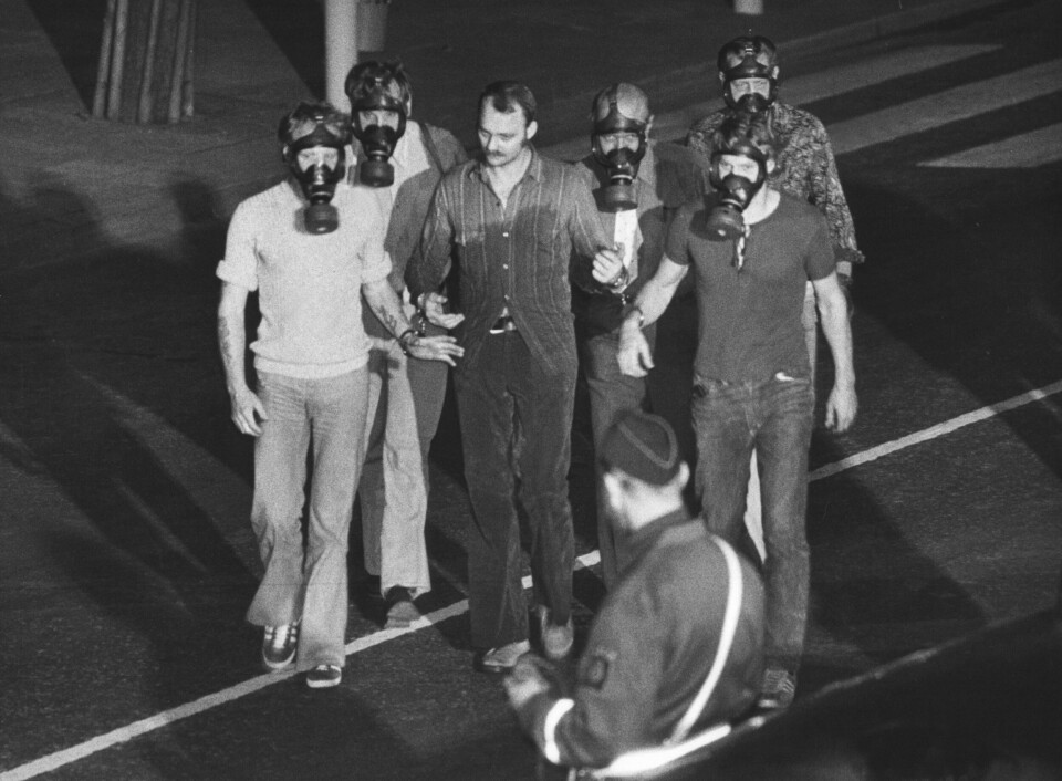 TRIUMF I GASSMASKE: Politimenn paraderte bankraneren Janne Olsson foran pressen etter pågripelsen i bankhvelvet. De våte klærne skyldtes at tåregassen tvang Olsson ned på golvet, som var vått av kjølevannet fra bormaskinene.