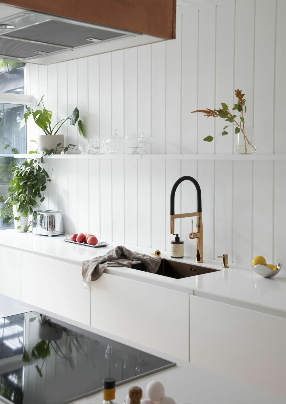 Overskap er valgt bort i det relativt lille rommet, for å ivareta lys og luft. De åpne hyllene gir mulighet til å lage litt miljø på den hvite veggflaten. Kjøkkenvasken er Lavabo Kubus, armaturen Essence fra Grohe og hvitevarene fra Miele.