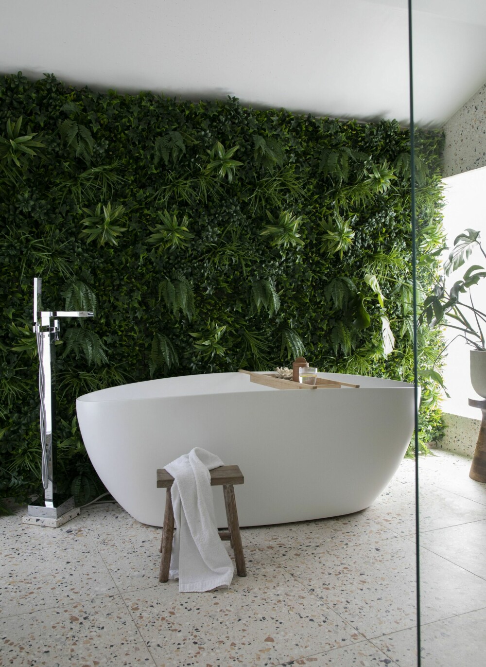 Den grønne veggen med kunstige planter gir badet et visuelt løft. Korab og Marsona elsker veggen som de har laget selv, satt sammen av ferdige kvadrater fra Green Plant Walls. Badekaret og armaturen er kjøpt hos AliExpress, og terrazzoflisene er fra Modena.             