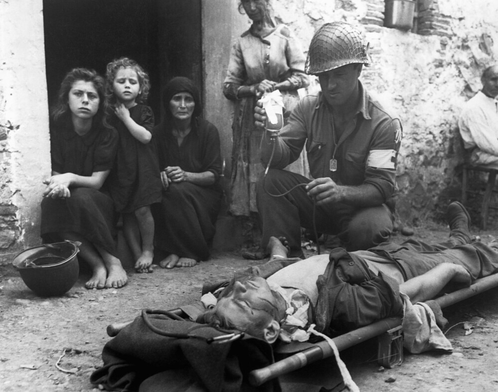 <b>KRIGENS MANGE ANSIKTER:</b> Det mest berømte bildet fra kampene på Sicilia. Sivile fulgte med på sanitetssoldaten Harvey White som forsøkte å redde livet til en såret medsoldat, Roy Humphrey. Det lyktes ikke.