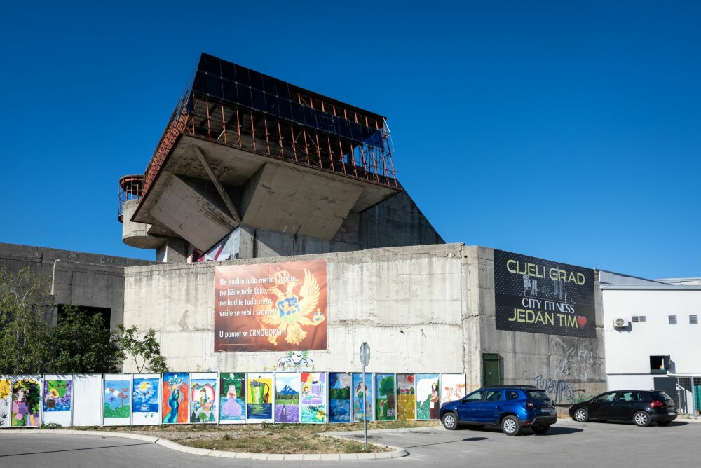 <b>REVOLUSJONENS HUS:</b> Dom Revolucije i Nikšić. Trappeoppganger og innganger er blokkert med et grønt stålgjerde. Den grå betongen har blitt delvis dekket av graffiti og reklame.