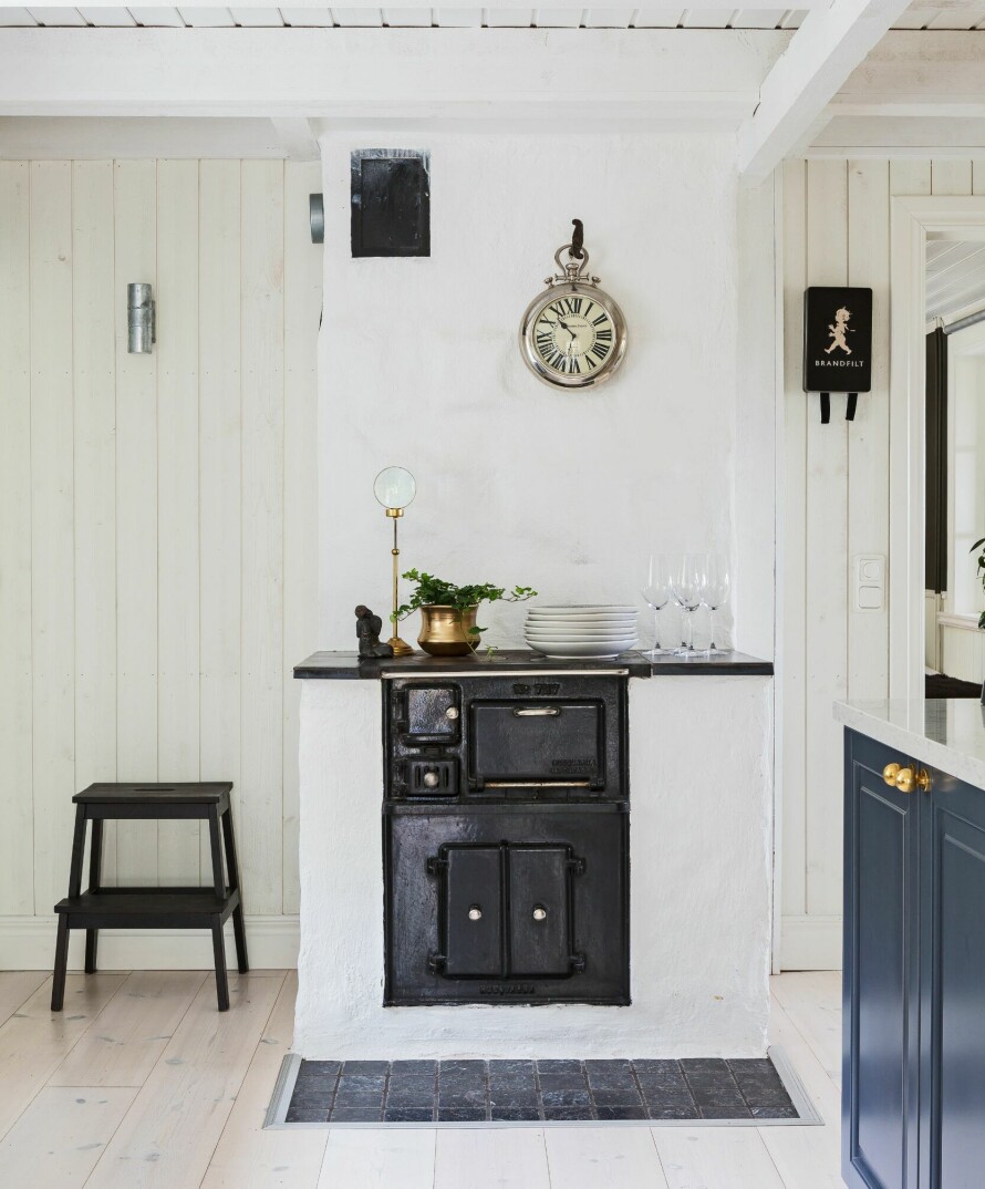 ORIGINAL VEDKOMFYR: Den flotte vedfyrte komfyren er en Husqvarna fra 1924. Klokken på muren bak kommer fra den nedlagte butikken Hans Mikaels. Krukken er et loppefunn som er spraymalt med gullfarge. Lysestake fra Blomsterlandet. Buddhastatuen er kjøpt i Frankrike.