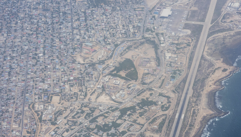 Fra luften: Utsikt over Mogadishu fra flyet. Det går en linje i Mogadishu mellom «den trygge sonen» (på sjøsiden) og «den utrygge sonen» (hvor husene ligger kvadratisk, øverst til venstre). Flystripen til høyre.