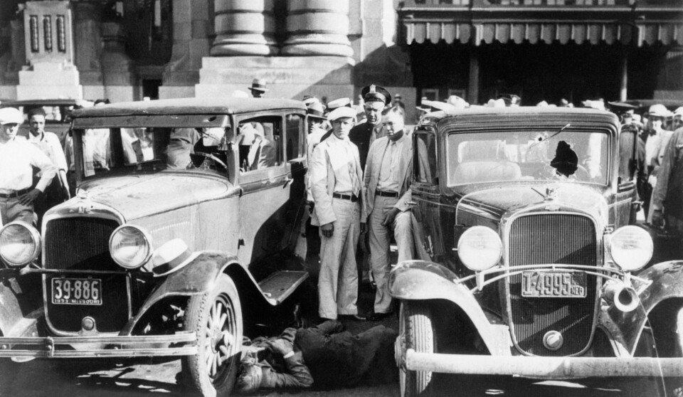 ETTER SKUDDENE: Politimenn poserer for pressefotografen mens ofrene fortsatt ligger strødd etter massakren i Kansas City. Angrepet kostet fem personer livet, tre av dem satt i bilen til høyre og to befant seg utenfor.