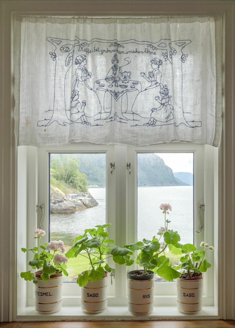 PERSONLIG: I krukkene som tilhører et spiserisett vokser yndige pelargoniaer. Vinduet er rammet inn av en nydelig håndsydd gardin med teksten Kaffe i det grønne kan umaken lønne. Den passer godt til Tone som har hagedilla.
