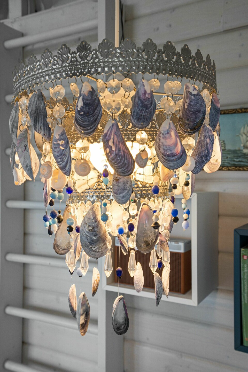LYSEKRONE AV SKJELL: Lampen over spisebordet er laget av Eirill. Det var i utgangspunktet en enkel takpendel med noen påsatte glasskrystaller. Disse er dels byttet ut med blåskjell som hun har plukket på stranden.