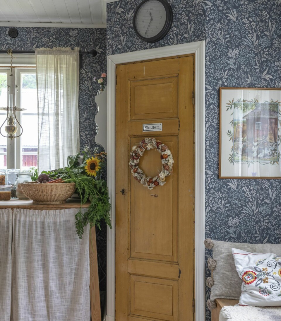 BRUKTFUNN: Den gule døren til spiskammeret er kjøpt brukt, og passet perfekt i hjørnet der de har bygd et helt nytt spiskammer. På døren henger en krans med egendyrkede blomster.