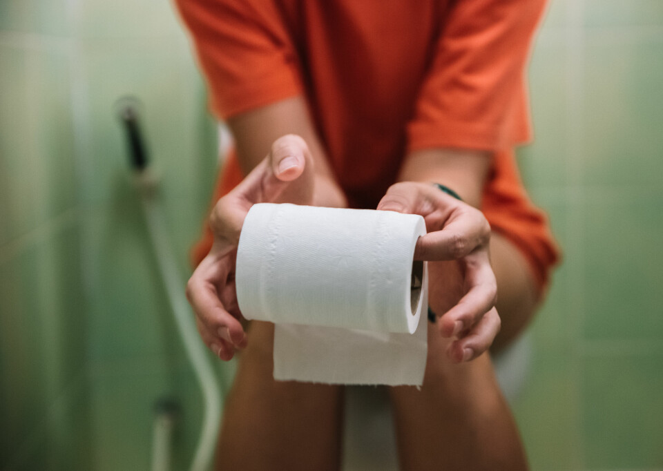 Woman sitting on toilet holding toilet paper roll