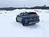 Mørk SUV parkert på snødekt område med skogkledd ås i bakgrunnen