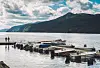 Småbåter ved brygge i norsk fjord med fjell og skyer i bakgrunnen