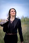 Kvinne i svart dress med horn over skulderen går i et åpent landskap