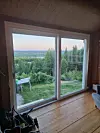 Stor glassdør med utsikt mot skog, åser og kveldshimmel