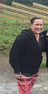 Smilende person i treningsklær står på en grusvei foran et gjerde.