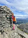Turgåer står ved stor steinvarde på fjelltopp med utsikt over dal og fjell