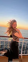Kvinne poserer ved rekkverket på et cruiseskip foran havet ved solnedgang