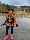 Kvinne i turklær og redningsvest står foran en snøfri alpinbakke